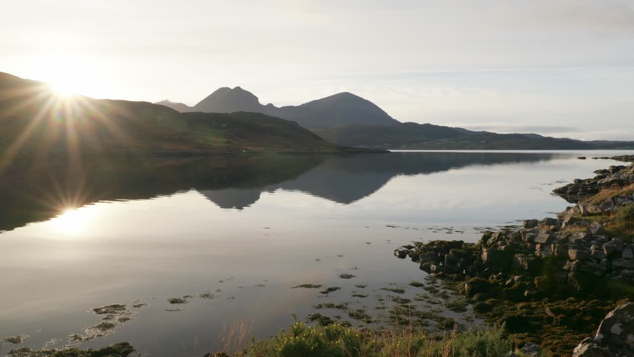A golden sunburst reflects off of the still surface of a tidal sea loch 