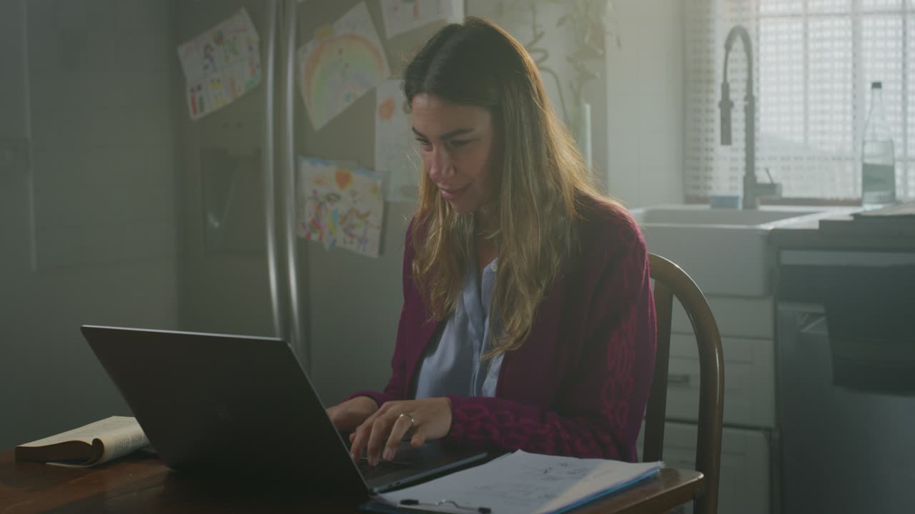 Imagem cinematográfica de jovem mulher de negócios e mãe sorrindo satisfeita enquanto faz teletrabalho com laptop de casa na cozinha durante o confinamento. Conceito de tecnologia, trabalho à distância, confinamento