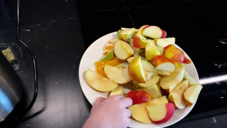 Vista-Superior-En-Cámara-Lenta,-El-Niño-Toma-Rodajas-De-Manzana-Del-Plato-Blanco,-Mano-Pequeña-Con-Frutas