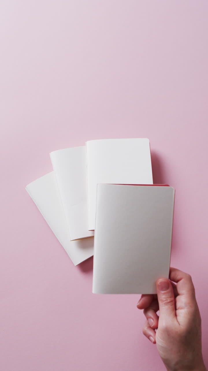 Vertical video of hand holding piece of paper over pieces of paper with copy space in slow motion