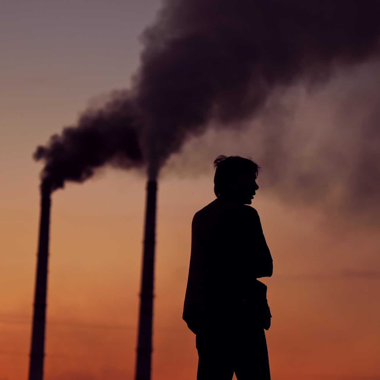 Silhouette of a man on the polluted air background. Evening sky with dark smoke going from industrial pipes and a man outdoors. Environmental pollution.