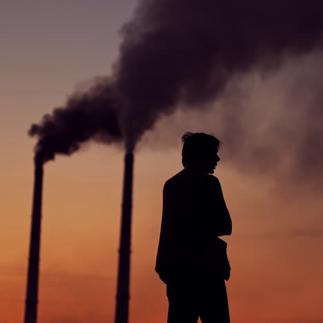 silhouette of a man on the polluted air background. evening sky with dark smoke going from industrial pipes and a man outdoors. environmental pollution.