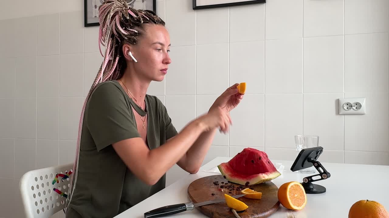 Giovane donna che taglia e mangia un'arancia fresca in cucina