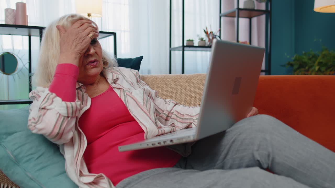 Stressed upset senior grandmother woman working on laptop computer received bad loss news at home