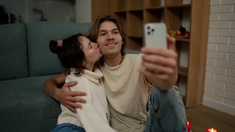 Encantadora-Pareja-Sentada-En-El-Suelo-Juntos,-Tomando-Selfie-Con-Smartphone