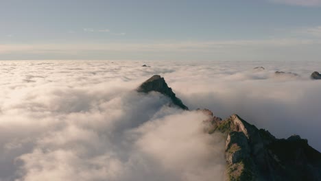 Clouds-almost-cover-entire-mountain-range-with-bright-sunshine,-aerial