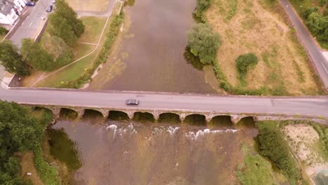 volando desde un hermoso río que fluye para revelar un viejo puente de ladrillo y una pequeña ciudad en el campo irlandés
