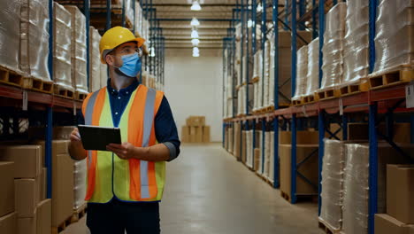 warehouse worker checking inventory with tablet and mask