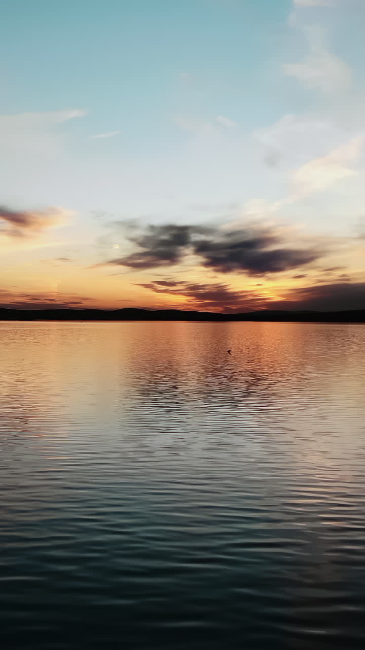 Superficie d'acqua calma che riflette un cielo colorato durante un bellissimo e pacifico tramonto su un lago