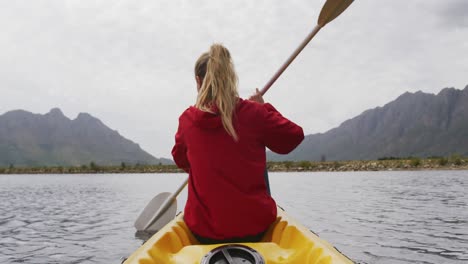 caucasian woman having a good time on a trip to the mountains, kayaking on a lake, holding a paddle