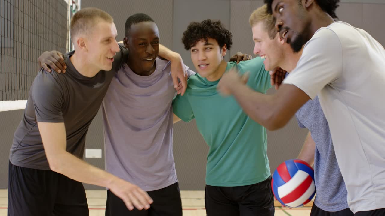 Diverse male team huddling in gym after rest, leader holding ball, stacking, planning then moving