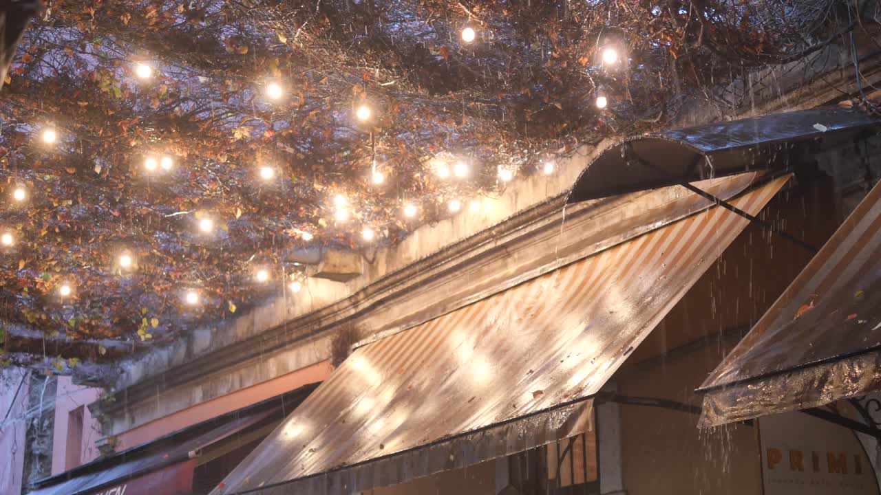 카페의 천막과 의 불빛으로 비가 오는 저녁 거리 장면