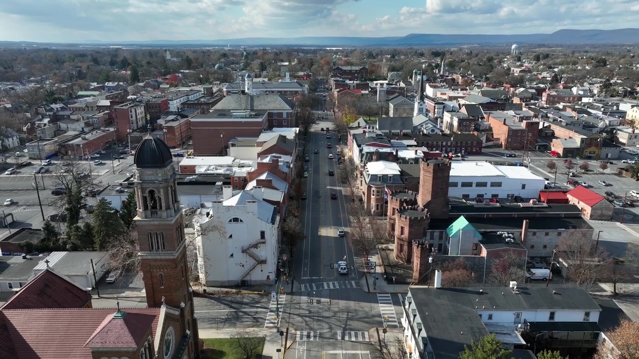 Ripresa aerea in allontanamento di una scena di traffico su una strada principale americana. Campanile della chiesa ed edifici storici in autunno. Ripresa a volo d'uccello. Carlisle City, PA, USA.