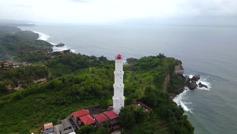 Tall-white-lighthouse-overlooking-rocky-cliffs-warning-passing-ships,-Indian-Ocean,-Indonesia