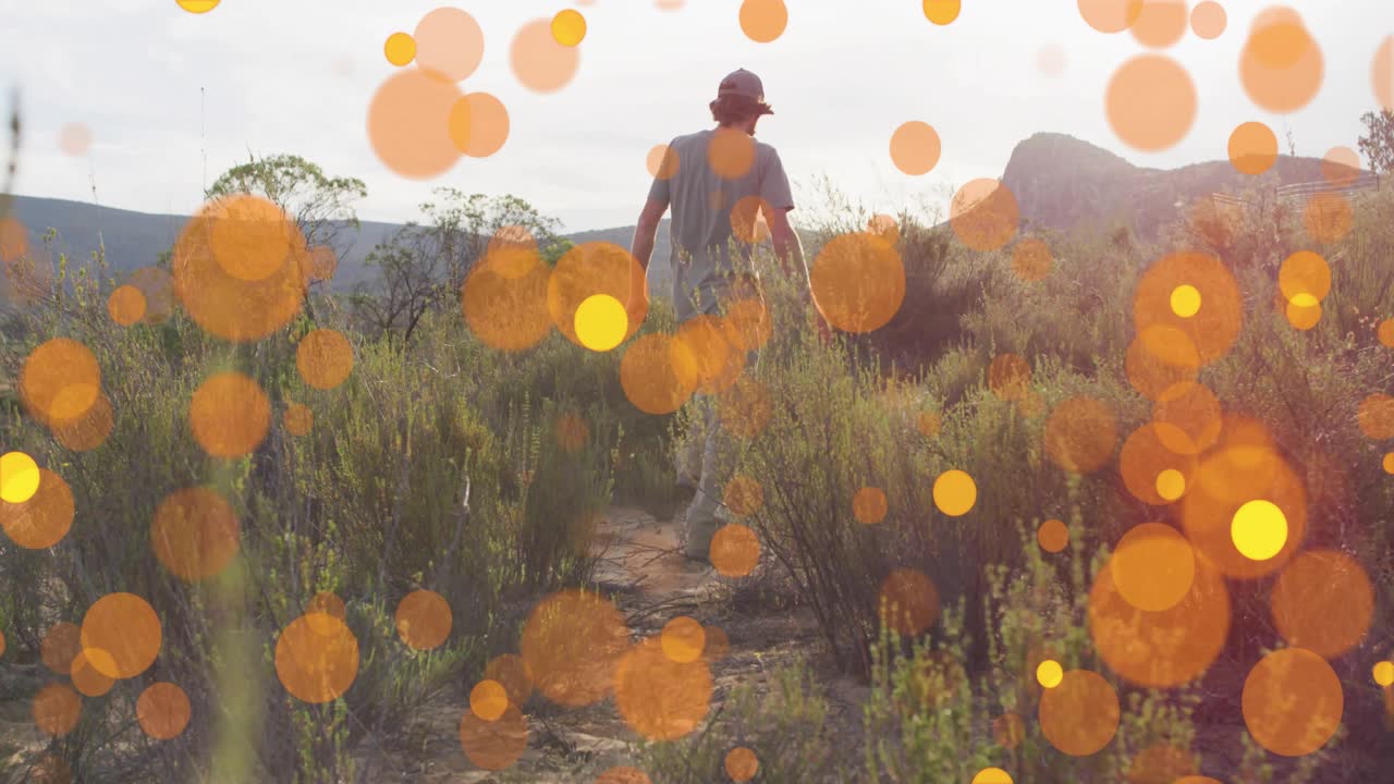 Excursionista masculino explorando un sendero del desierto mientras puntos bokeh naranjas animados emergen y mejoran anuncios de viajes