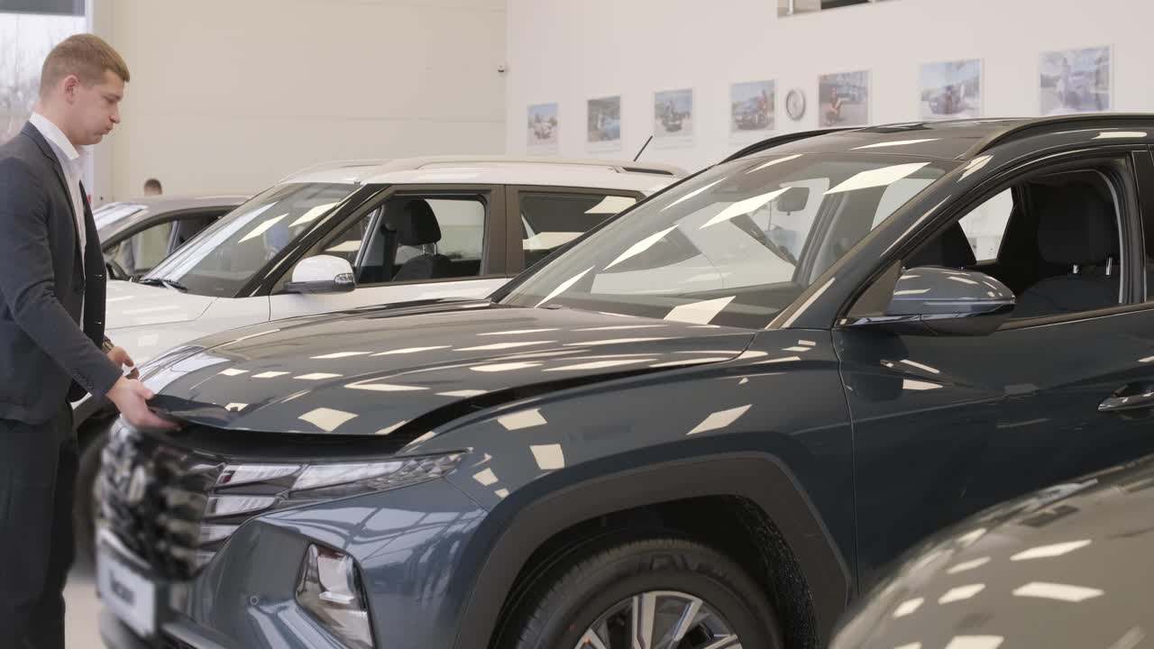 Hombre examinando el motor de un automóvil nuevo en el concesionario de automóviles mirando debajo del capó