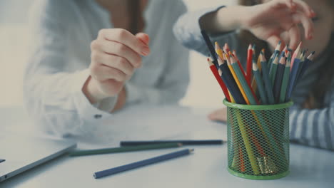 Mother-helps-little-girl-to-do-homework-with-colored-pencils.-Close-up.