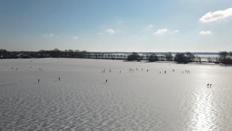 Aerial-drone-shot-over-frozen-lake-during-cold-winter-day-with-kids-ice-skating-during-sunlight