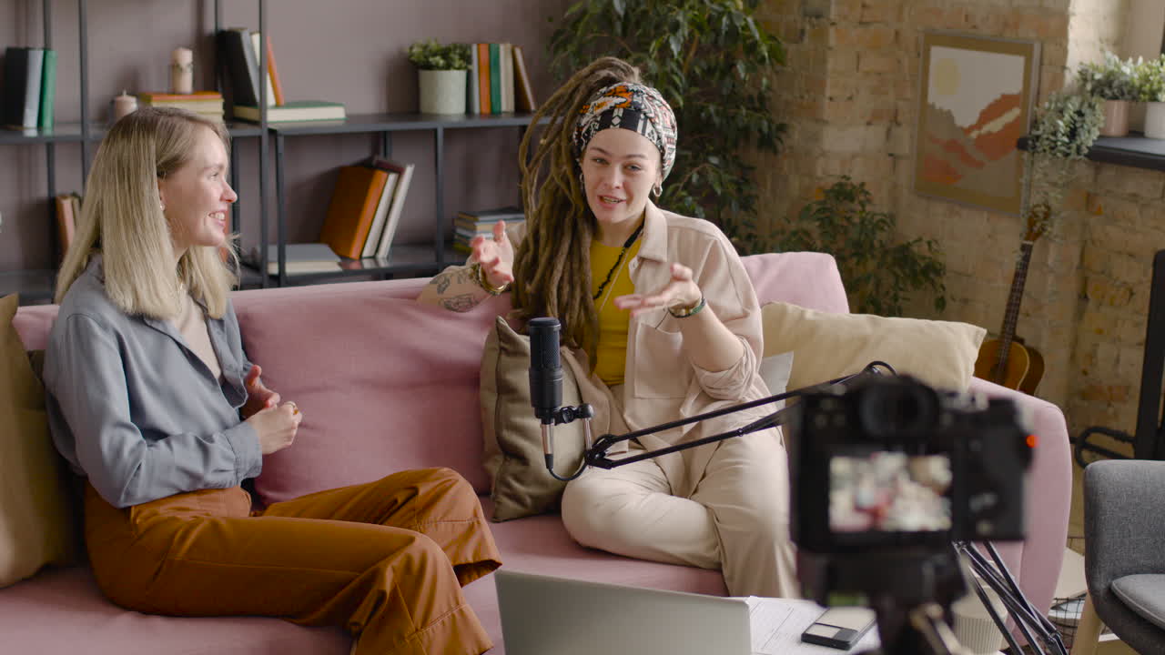 vista trasera de una cámara que está grabando a dos mujeres en un podcast hablando por un micrófono mientras están sentadas en el sofá 1