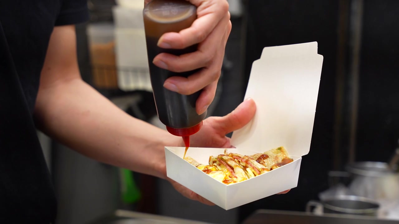 Street food vendor is pouring sauce on a Taiwanese egg pancake, Dan Bing, at a night market