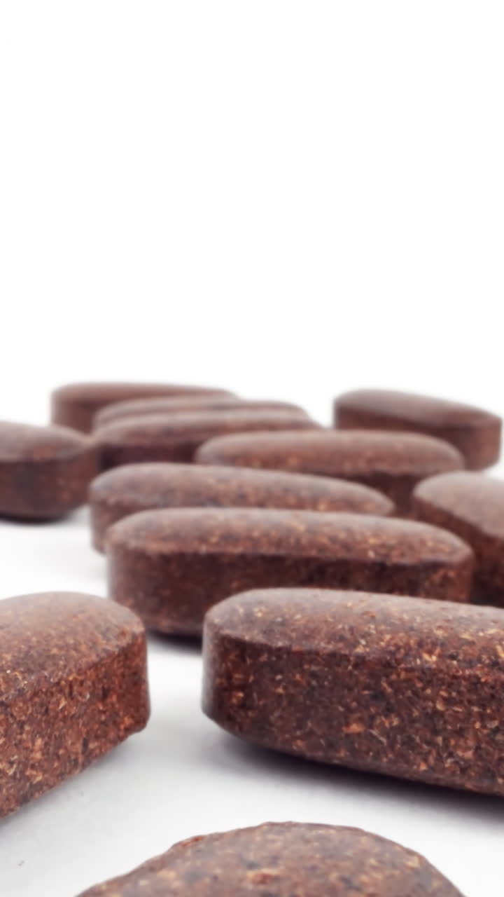 varios comprimidos marrones de hierbas en una superficie blanca con enfoque selectivo