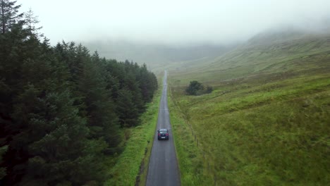 driving a car in an epic road in the middle of the mountains in ireland in a fog day