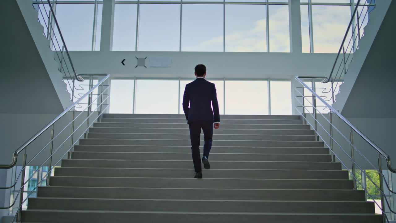 Elegant entrepreneur climbing stairs in modern office back view. Businessman