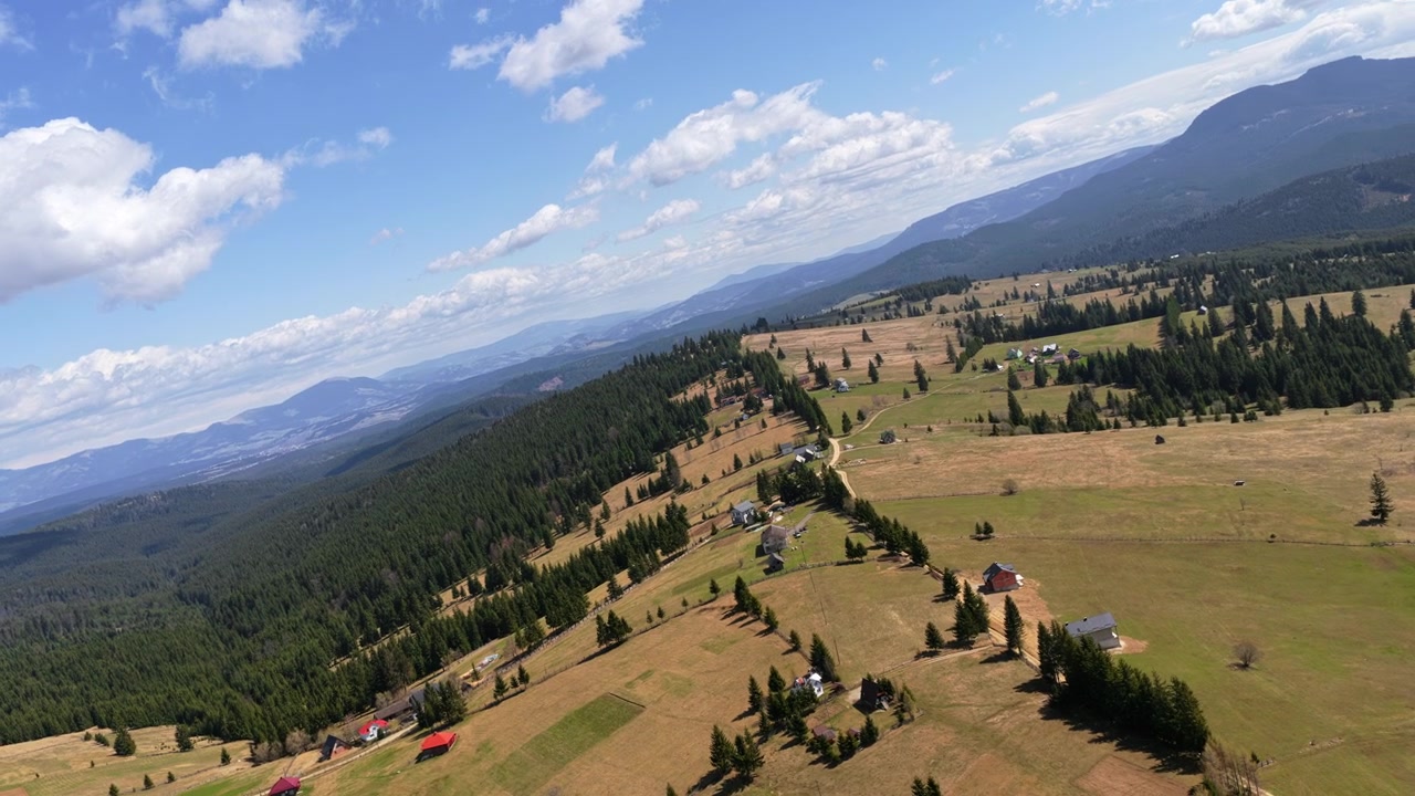 Vista aerea con drone di colline e piccoli insediamenti intorno a Vatra Dornei, che mostra terreni agricoli, foreste e paesaggi aperti tipici della Bucovina