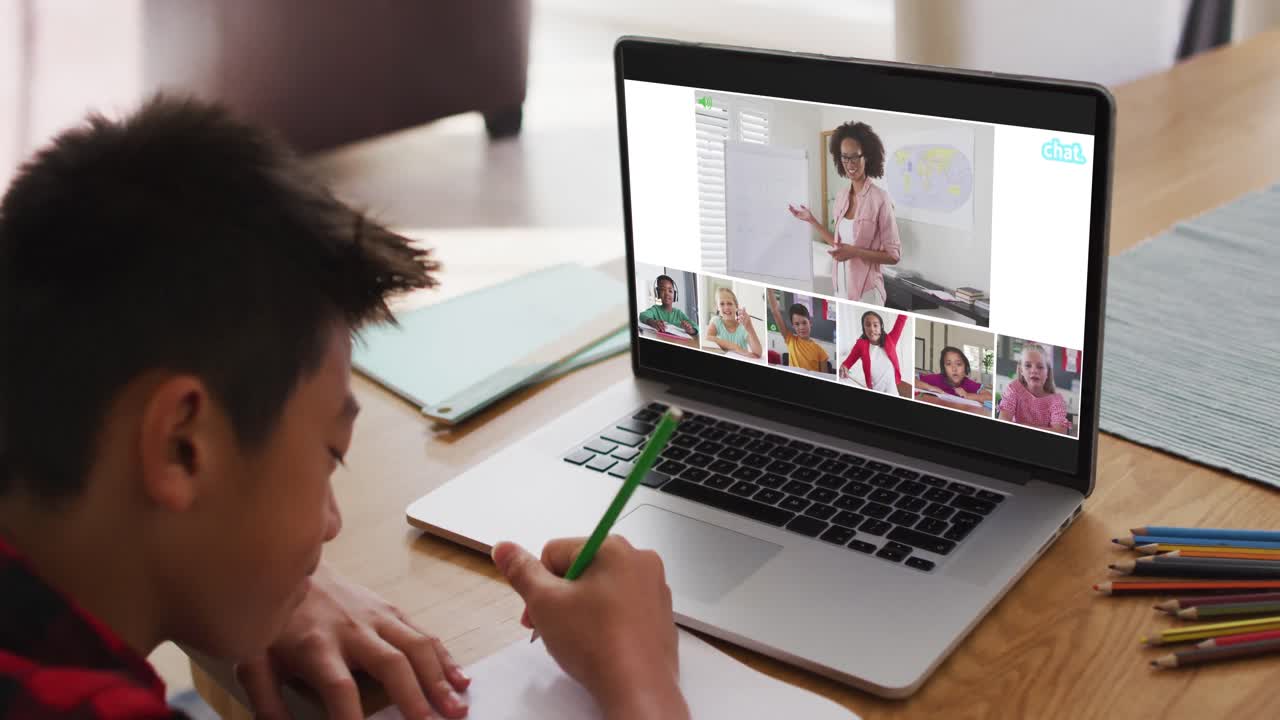 Schoolboy using laptop for online lesson at home, with diverse teacher and class on screen