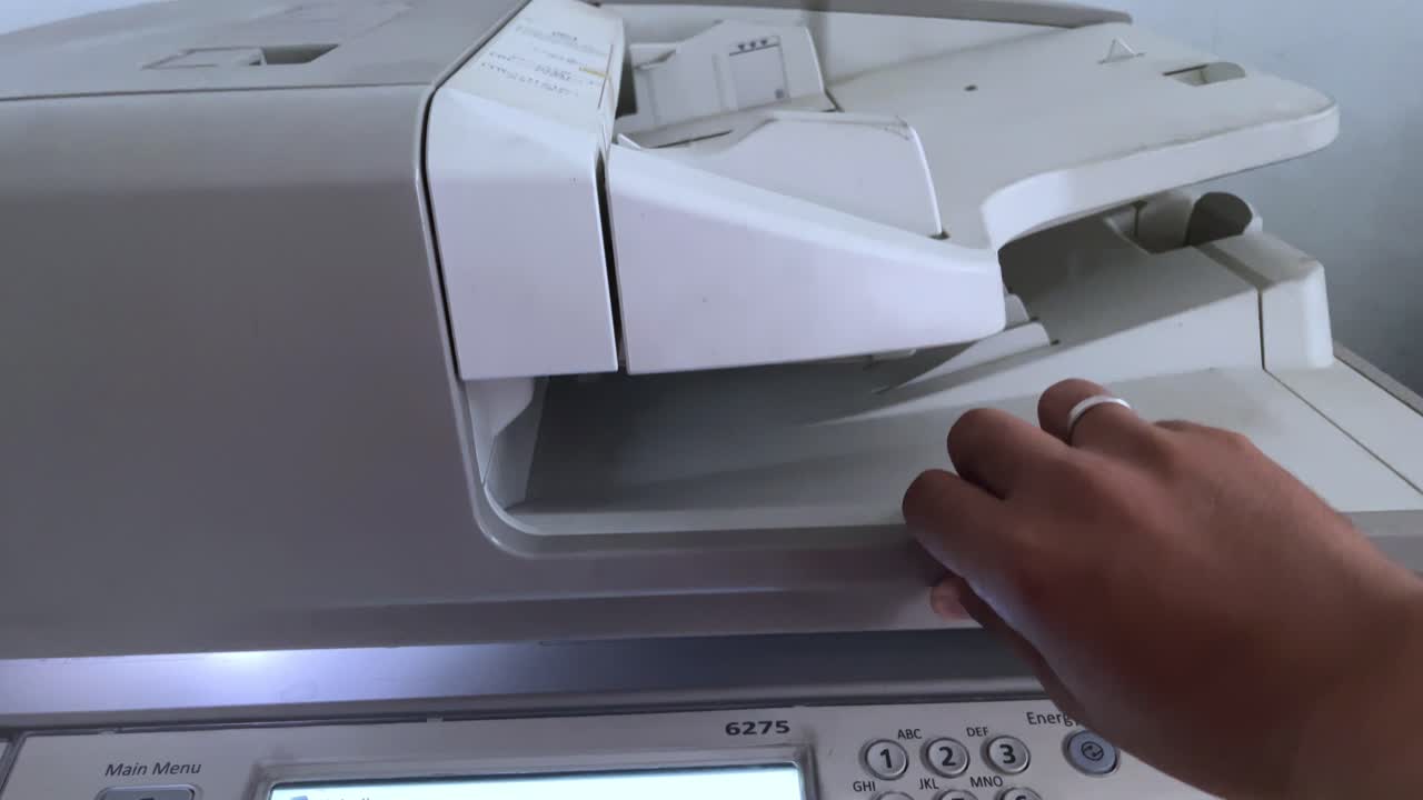A person's hand closes the photocopier cover to photocopy a file