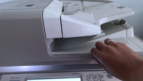 a person's hand closes the photocopier cover to photocopy a file