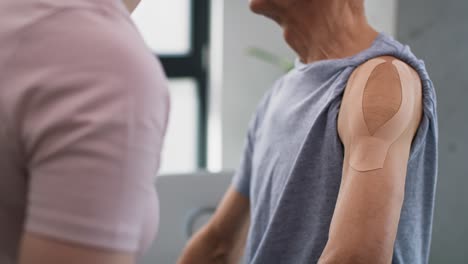 physical therapist applying kinesio tape on senior patient's arm.