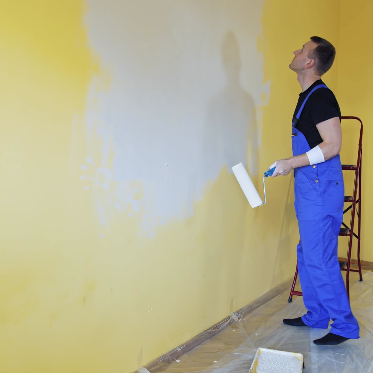 Handsome man with painting roller doing new indoor improvement. Professional builder renovating house
