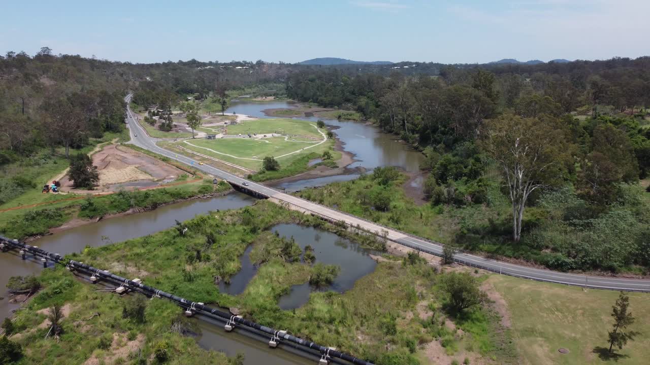 고속도로를 가로질러 초록색 공원을 향해 날아가는 드론과 최근 홍수 된 강을 가로지르는 파이프 라인 및 다리