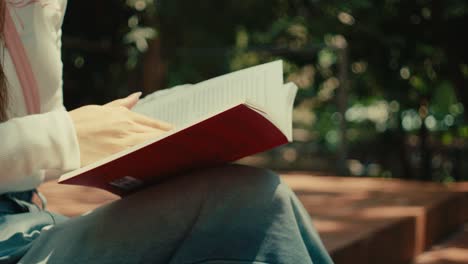 close up of woman girl hand turning the page of a book while sitting alone in a bench in the park reading a novel