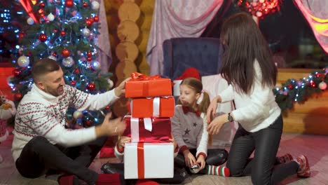 happy family with presents at christmas. parents and little girls spend time together in christmas decorated room. children with parents put gift boxes on the floor