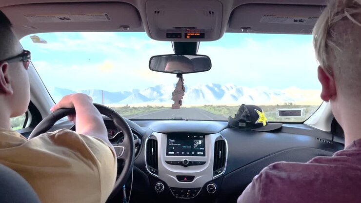 Driving in California through a barren landscape towards snow-covered mountain range