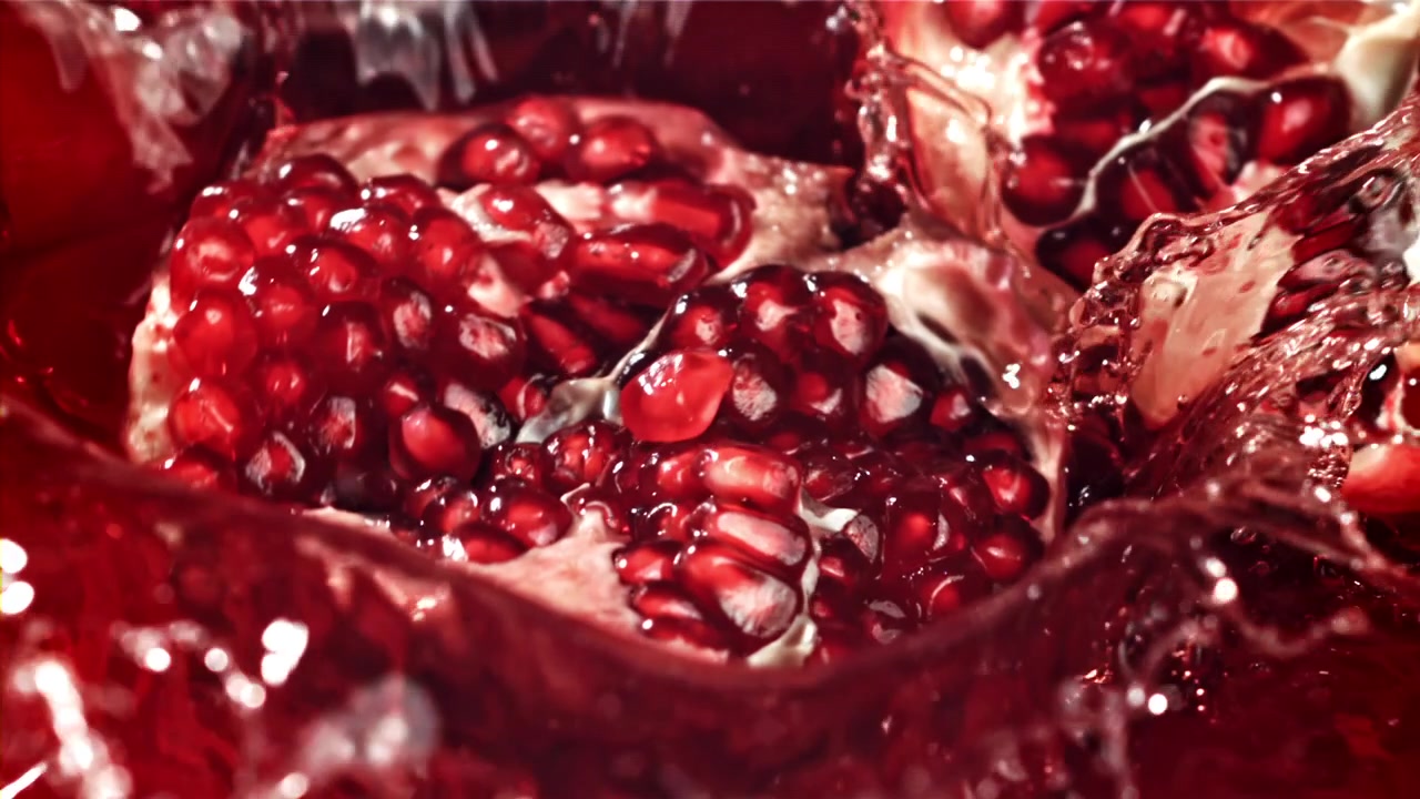 Slowmotion af granatæble, der sprøjter i rød saft