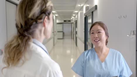 happy diverse female doctors talking in hospital corridor, turning and smiling, slow motion