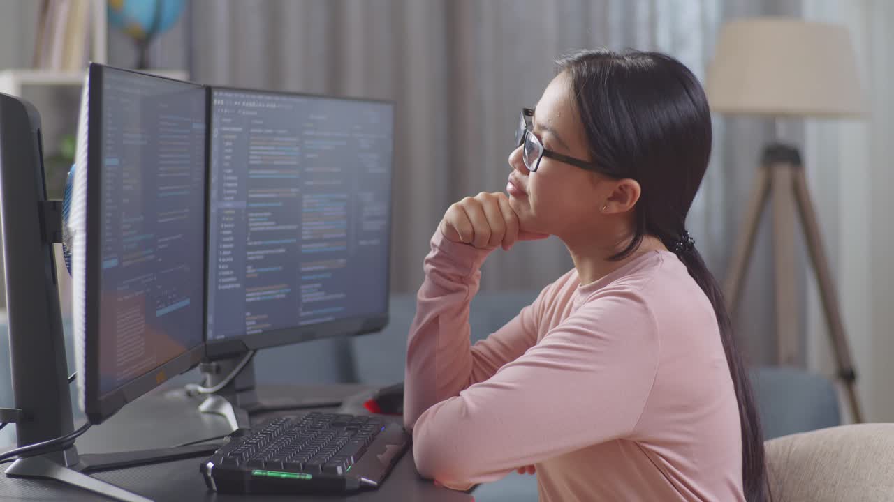 Asian Teen Girl Programmer Thinking About Something While Creating Software Engineer Developing App, Program, Video Game On Desktop Computer At Home. Terminal With Coding Language