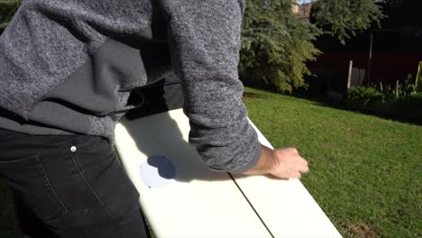 putting wax on the surfboard in the backyard