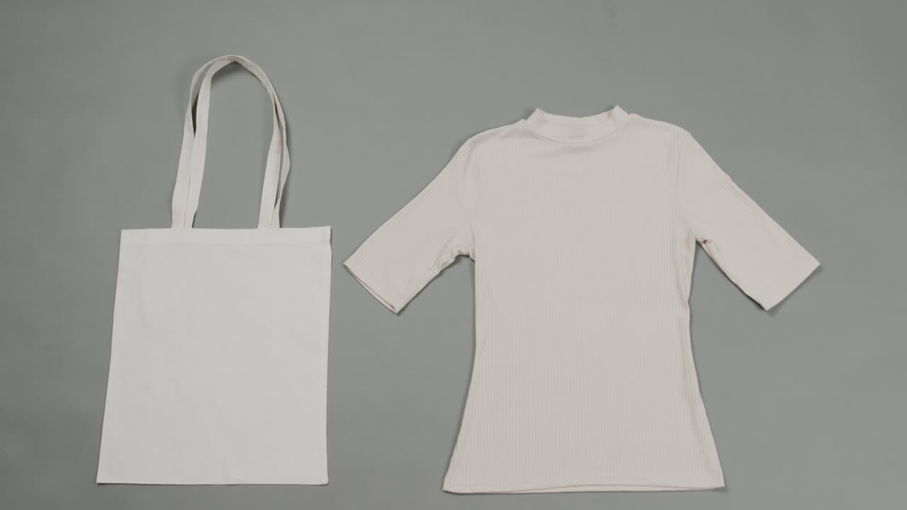 primer plano de una bolsa blanca y una camiseta sobre un fondo gris, con espacio de copia, cámara lenta