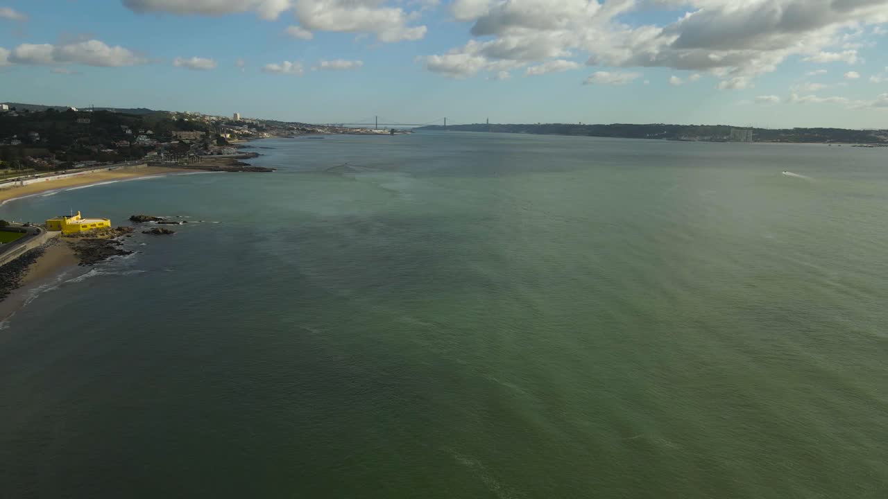 Filmato aereo soleggiato della costa di Caxias in Portogallo con acqua verde-blu e il ponte 25 de Abril visibile sull'estuario del Tago