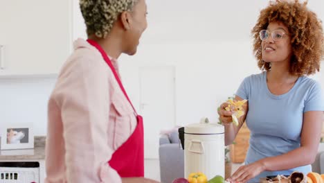 Happy-diverse-female-lesbian-couple-throwing-waste-out-and-cooking-in-kitchen-in-slow-motion