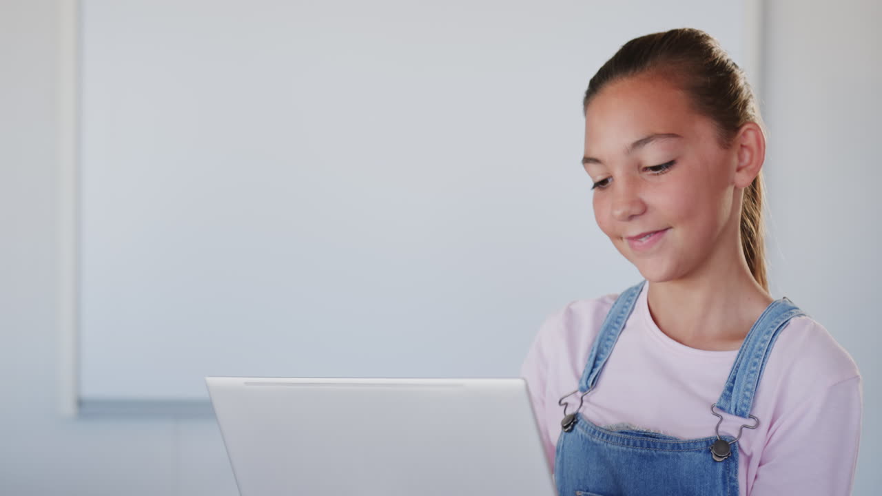 Smiling girl holding laptop in school classroom, ready for learning, copy space