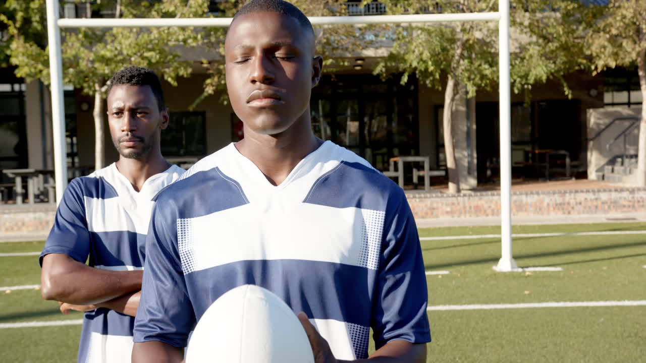 Holding rugby ball, young african american male athletes standing on sports field, ready to play
