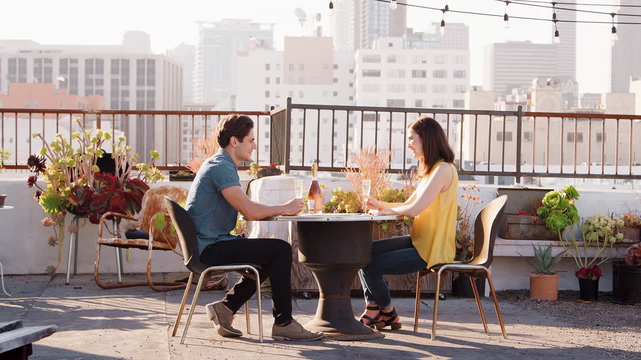 pareja bebiendo vino y haciendo brindis en la terraza de la azotea con el horizonte de la ciudad en el fondo