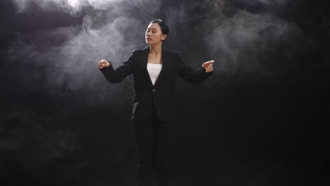 asian conductor woman holding a baton and showing gesture quickly in the black studio with fog