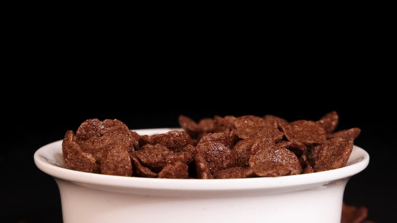 A hand reaches into a bowl of chocolate cereal against a black background, creating a dynamic and engaging scene