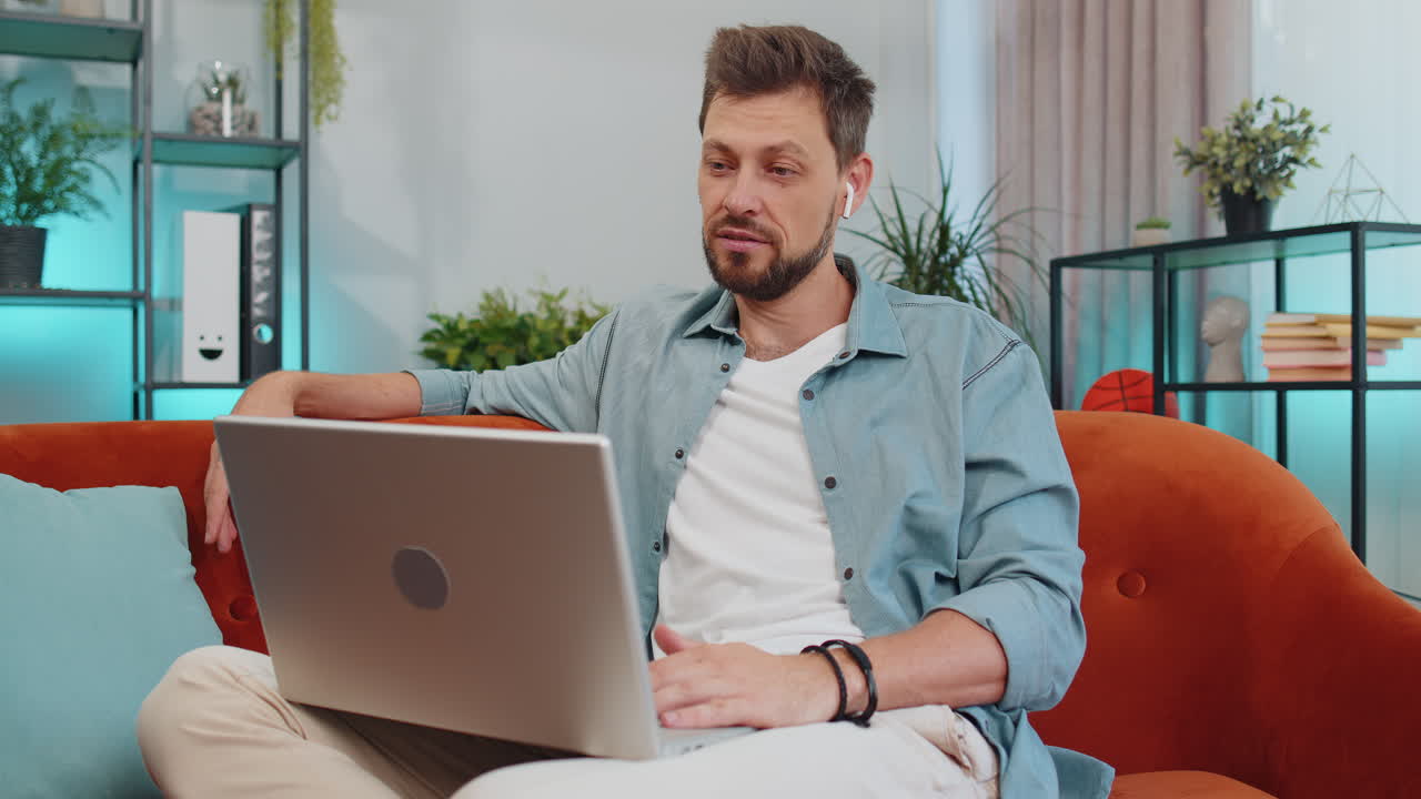 hombre sentado en el sofá de casa, mirando a la cámara, haciendo una llamada de videoconferencia con amigos o familiares